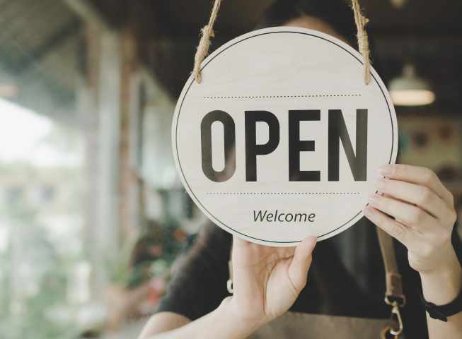 a store owner holding an open, welcome sign