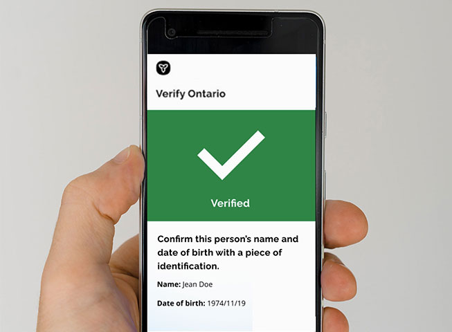 a hand holding a smart phone with a verify ontario check mark
