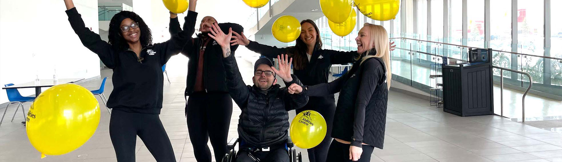 Abilities Centre Staff celebrate in the Atrium with their hands in the air while balloons float in the air 
