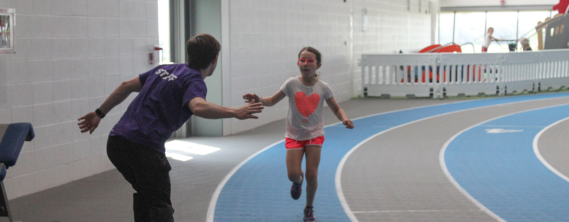 a youth running on track in Fieldhouse getting a high five from an Abilities Centre coordinator