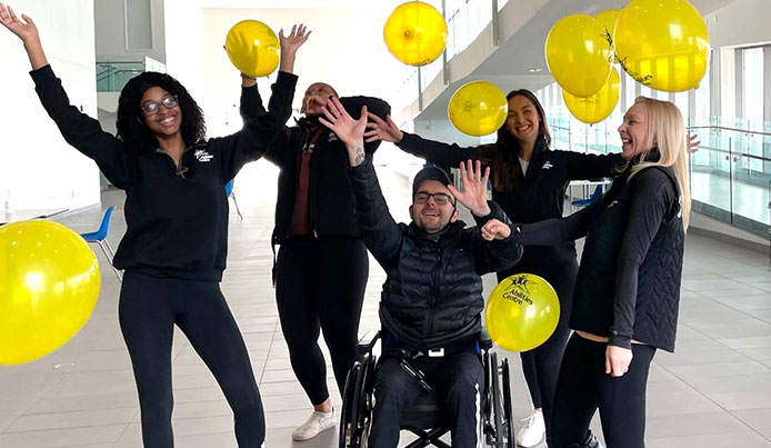 abilities centre staff celebrate in the atrium with their hands up in the air while balloons fall to the ground