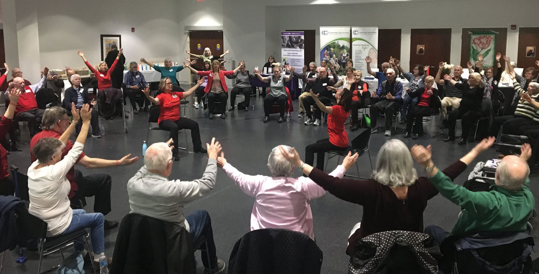 Program Coordinators leading group of multi-generational participants in a seated exercise routine 