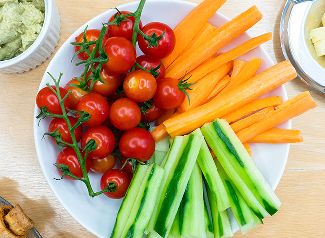 a fresh plate of cut vegetables including carrots, cucmber, and tomatos 