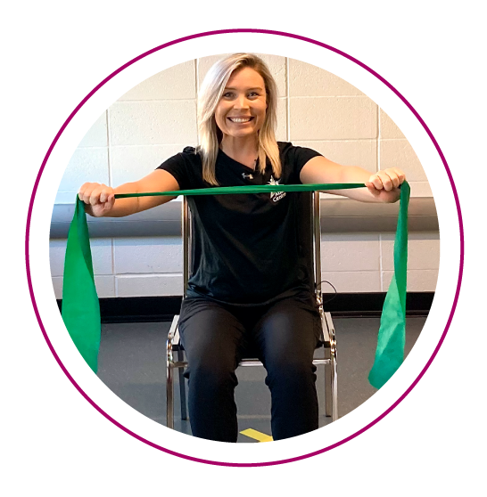 A trainer sits in a chair holding a green resistance band