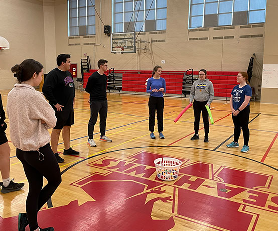 Participants stand in a gym preparing for an activity with the instructor