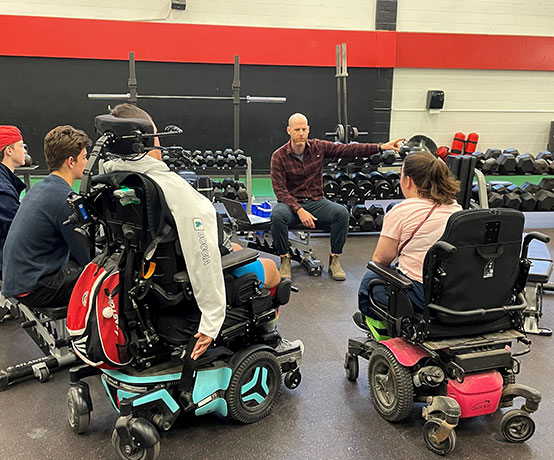 two people using mobility scooters and three others sit on benches talking about disability and inclusion