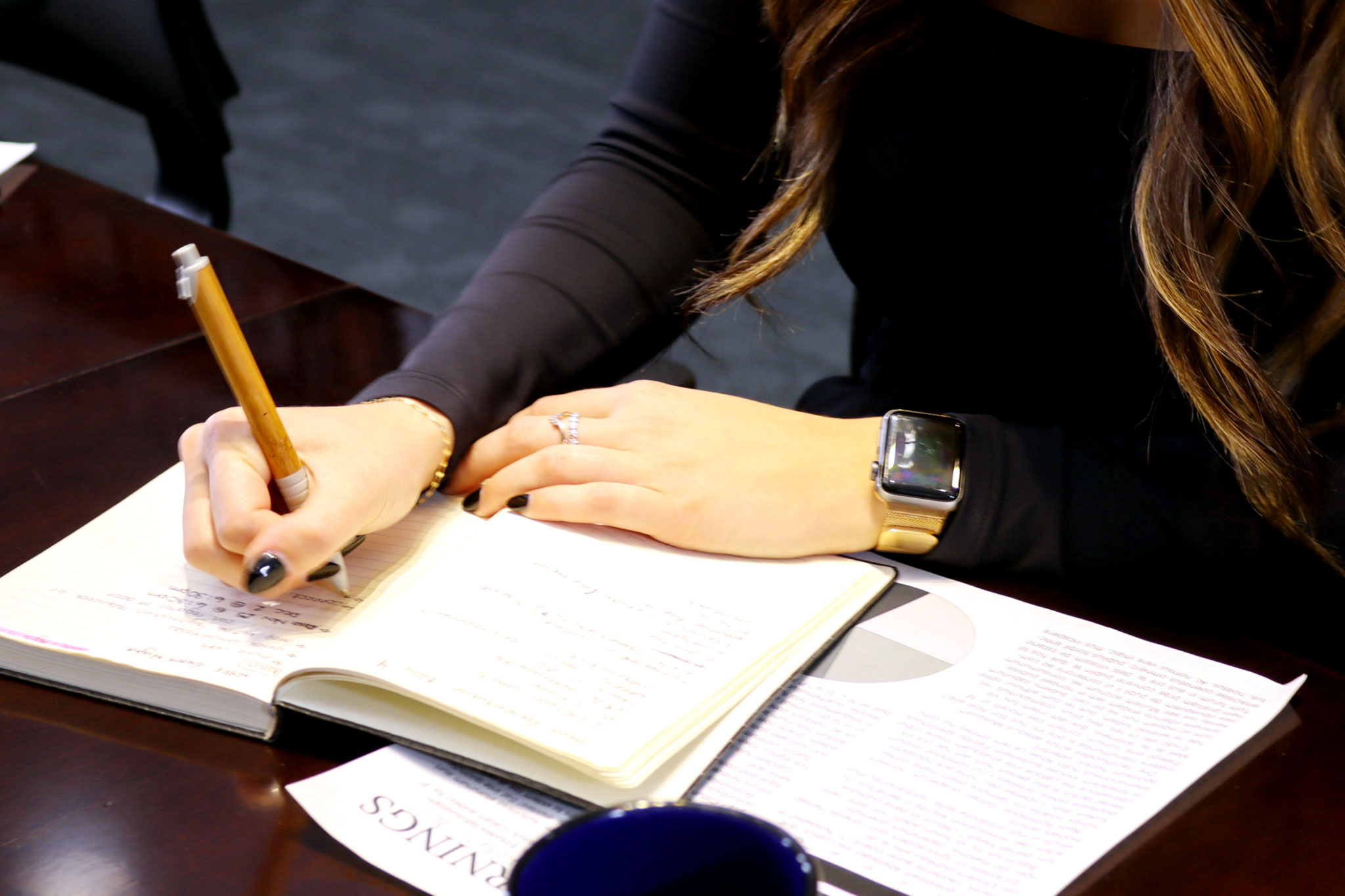 a person writing in a notebook sitting at a desk 