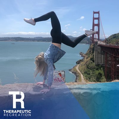Kaitlin does a handstand on a mountain with water and a bridge in the background