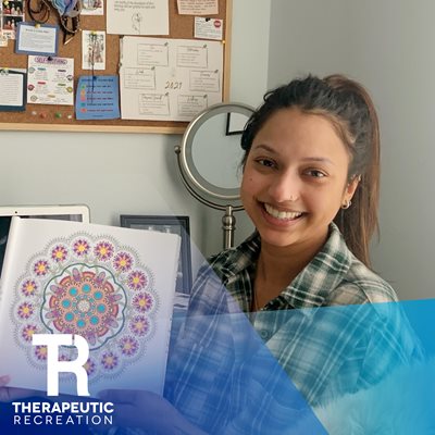 Nicole smiles sitting at her desk holding up a piece of her abstract artwork