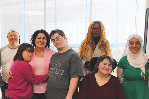 Picture of seven individuals in a group photo representing various ages, gender, ethnicity and disabilities