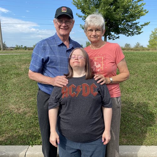 Alayne (centre) with her dad and mom behind her poses in the parking lot of Abilities Centre