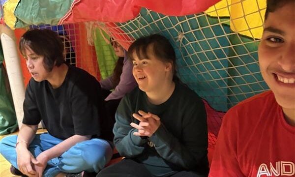 Three participants smile as they sit in a goal net.