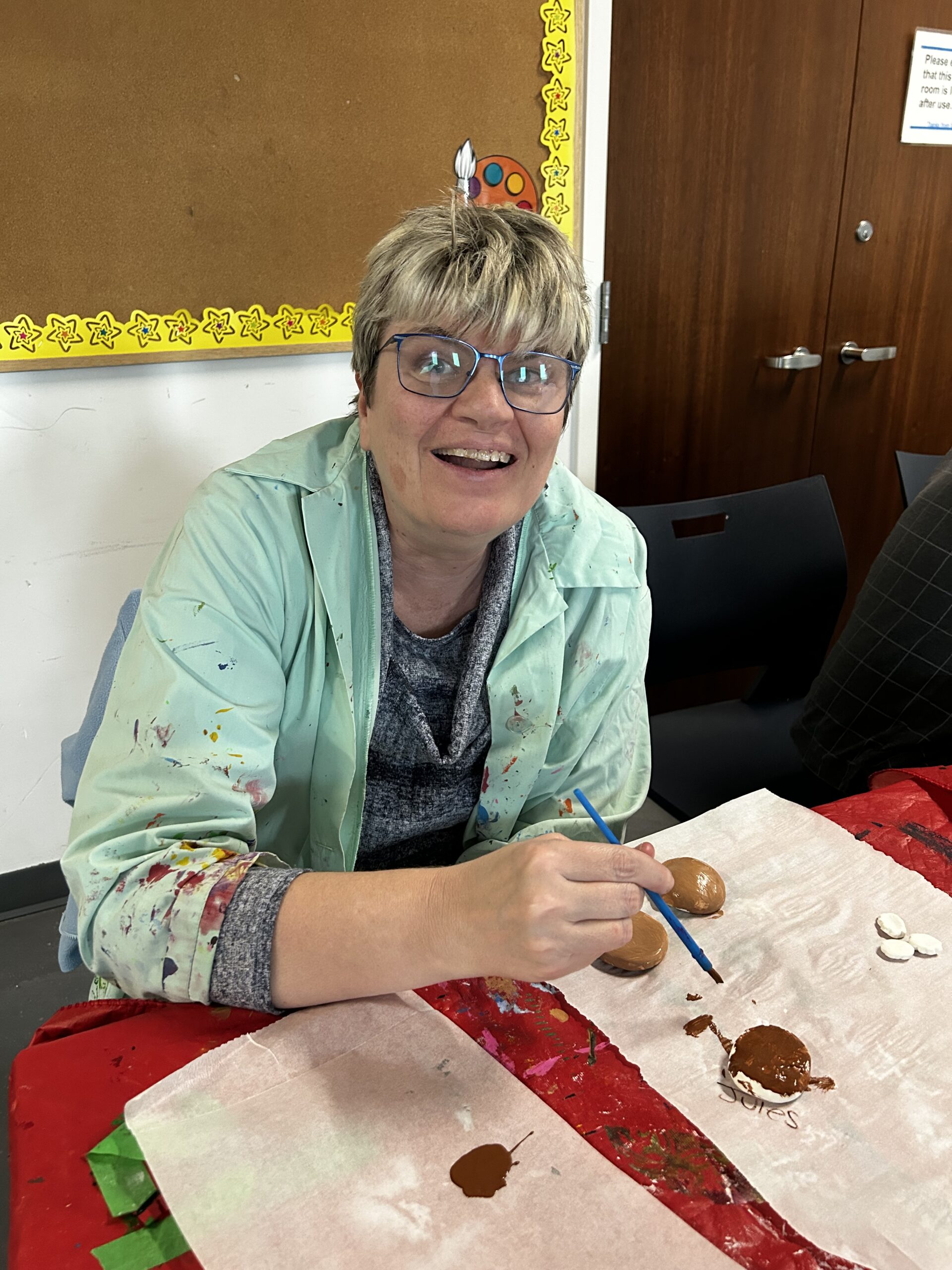 A woman smiles while painting rocks.