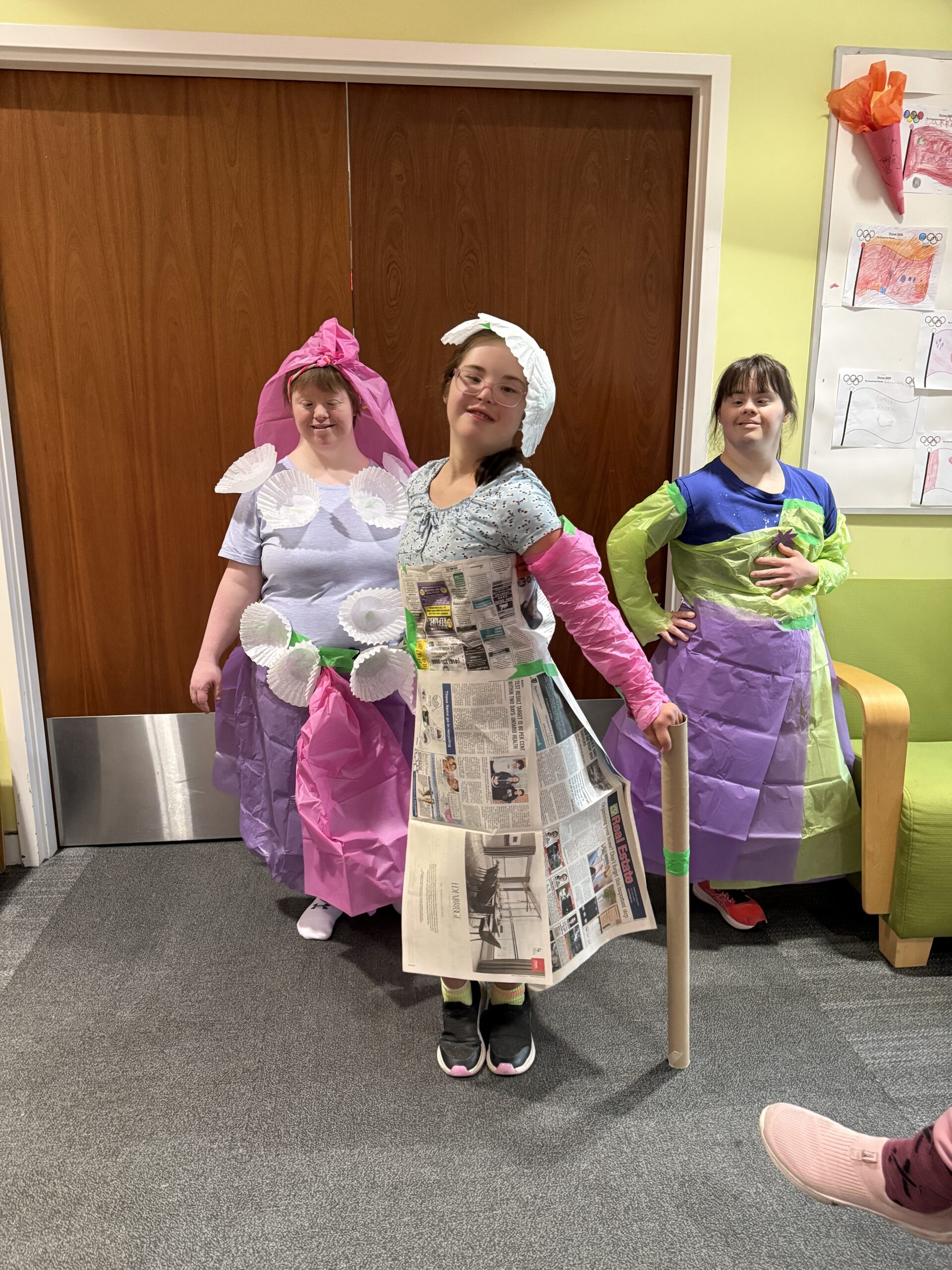 Three women are beaming as they pose in their paper and craft-designed outfits.