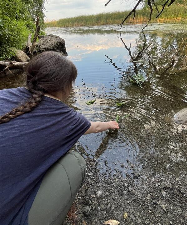 Someone bending down and putting their hands in the creek.