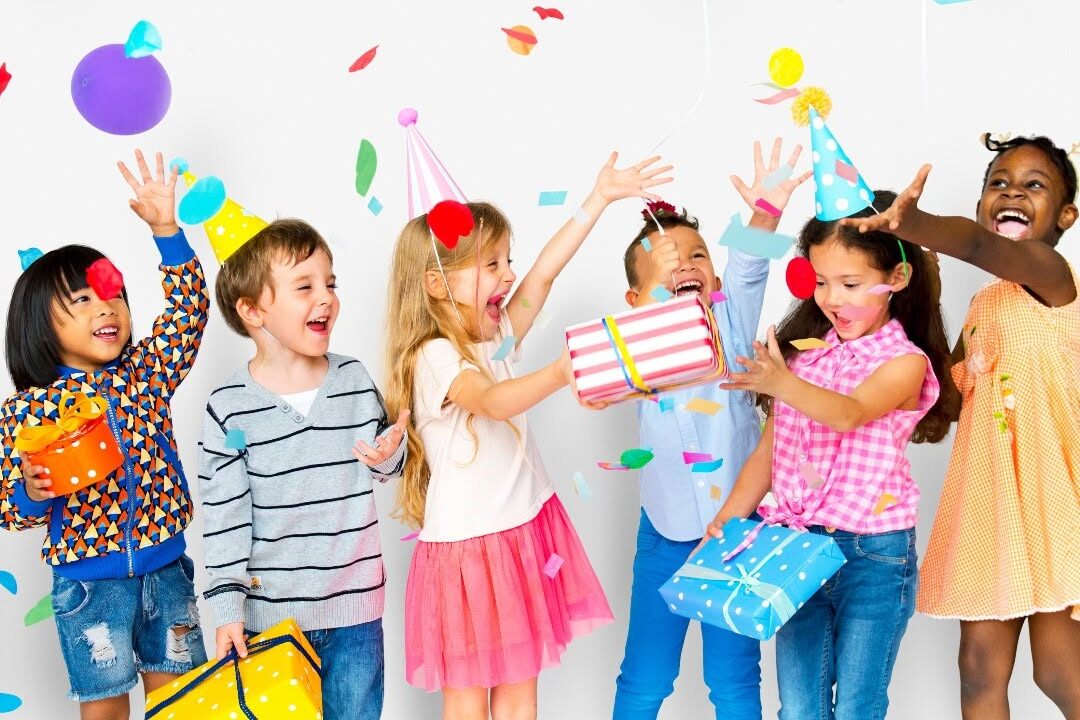 Children smile and cheer as they hold gifts during a birthday party.