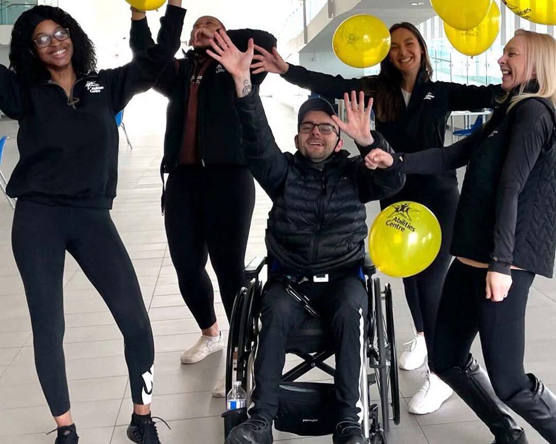 Abilities Centre staff smile and cheer as yellow-branded balloons fall.