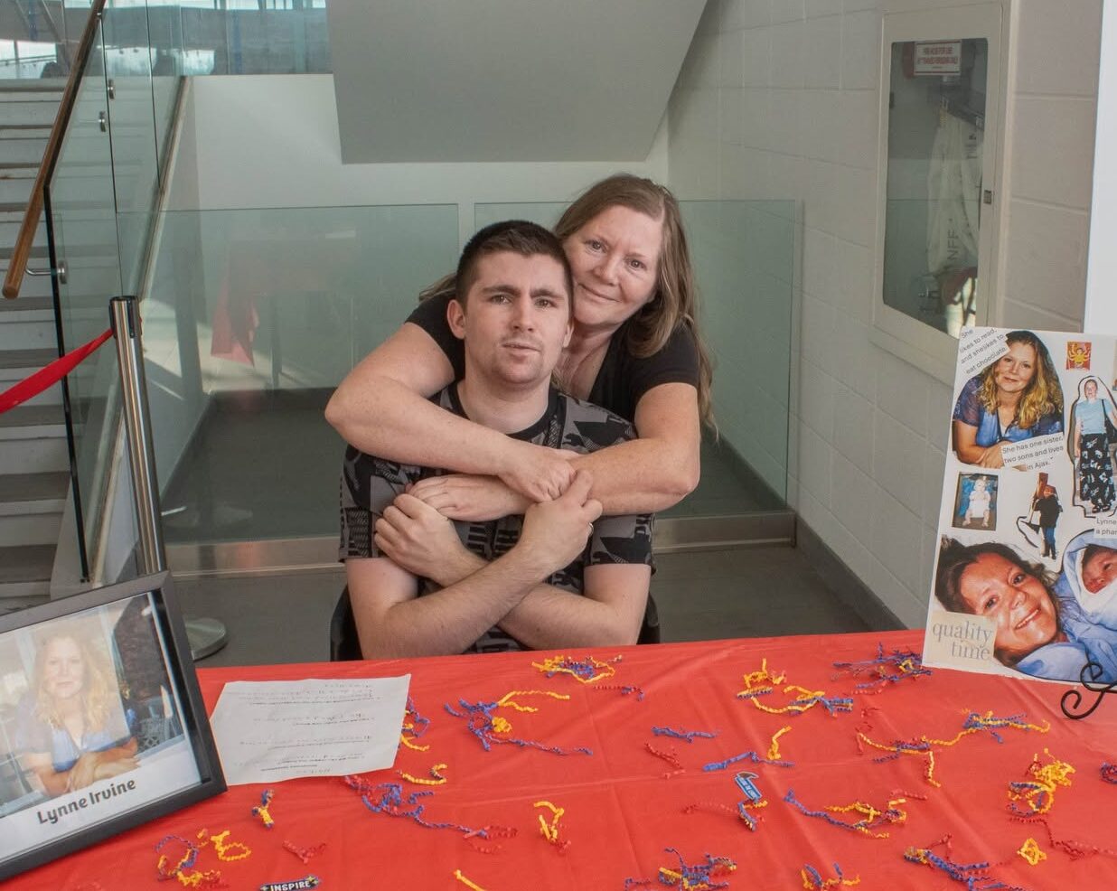 A woman hugs her son behind a table.