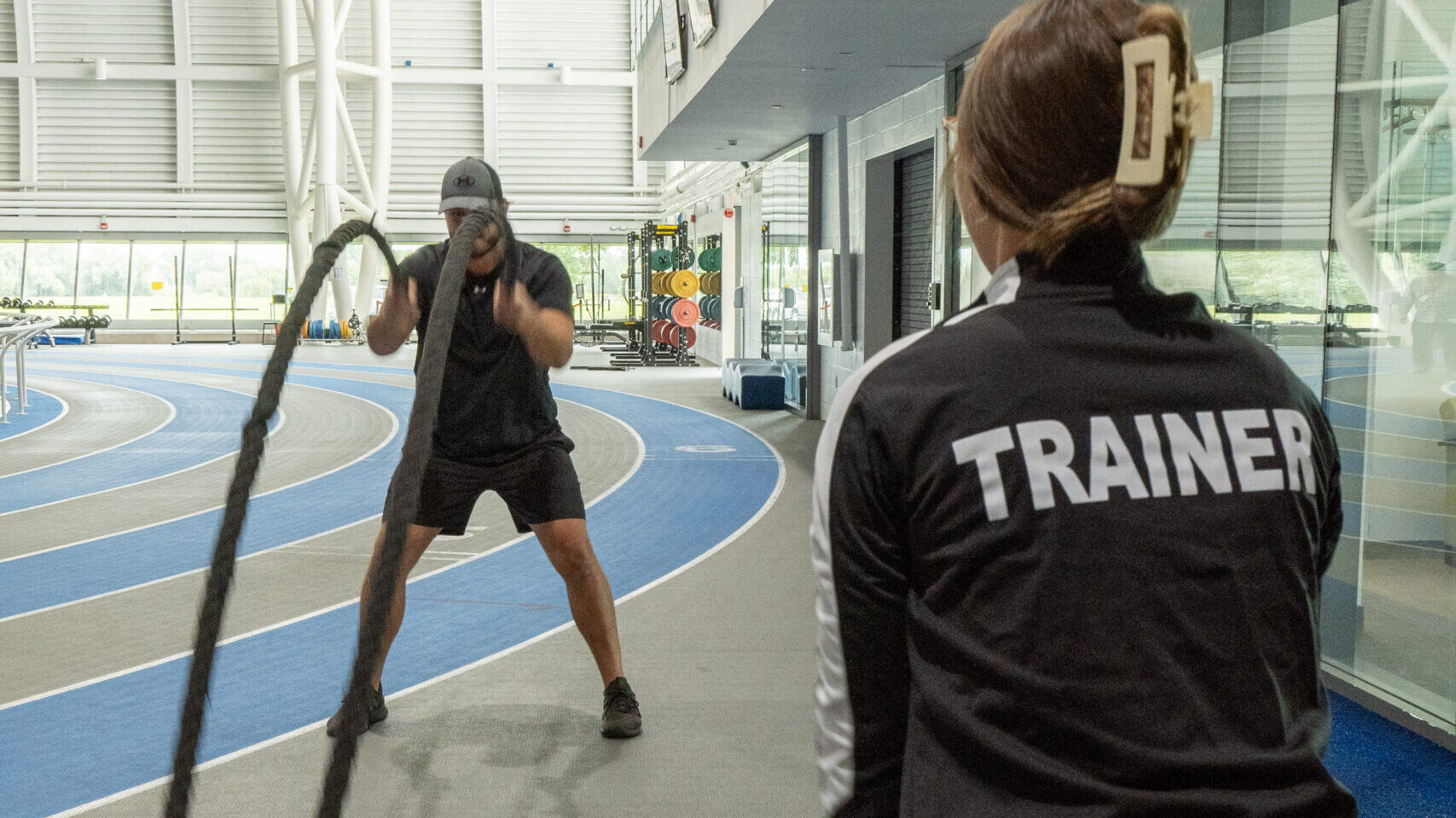 A trainer watches her client use the battle ropes.