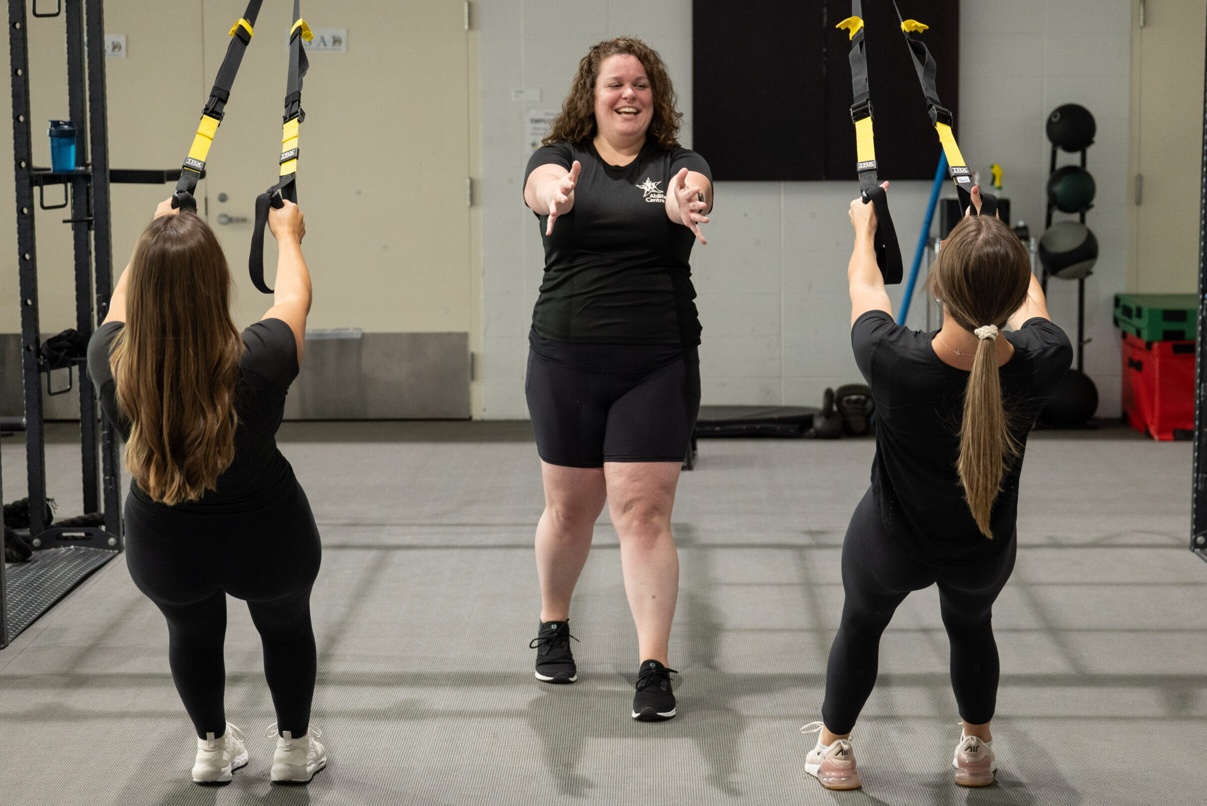 A trainer showing two clients how to use the T.R.X. machine.