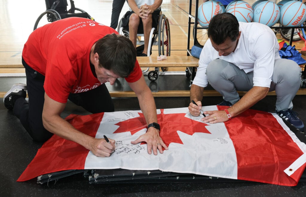 M.P. Ryan Turnbull and the Honourable Adam van Koeverden sign a Canadian flag.